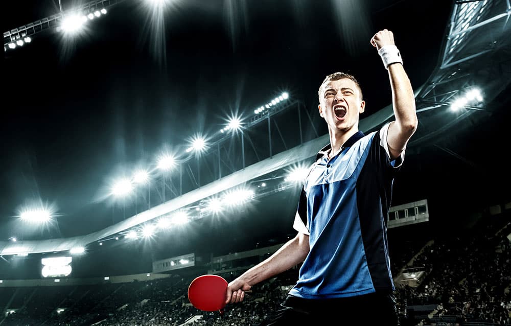 Home Junger Tischtennisspieler jubelt im Scheinwerferlicht eines vollen Stadions mit erhobener Faust.