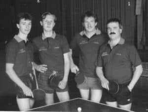 Schwarzweiß-Foto: Vier Männer im Tischtennis-Outfit, nostalgische 70er-80er Jahre, Teamgeist.