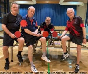 Seniorentischtennis: Vier Männer in Sportkleidung feiern Freundschaft und Spielfreude in heller Halle.