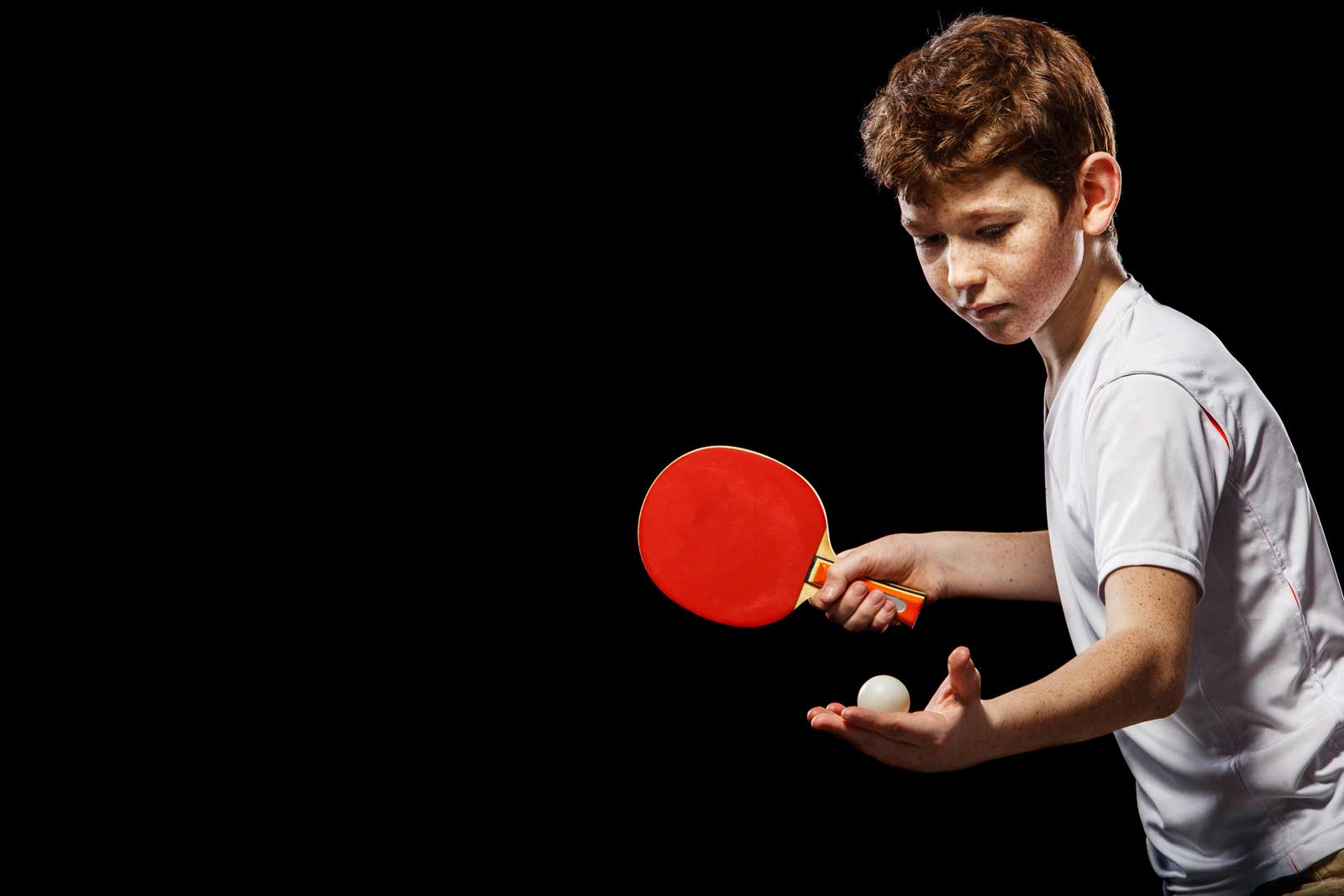 Home Junger Tischtennisspieler konzentriert sich intensiv auf den Aufschlag, vor schwarzem Hintergrund.
