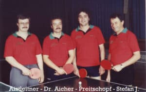 Vier Tischtennisspieler in roten Uniformen halten Schläger, fotografiert vor dunklem Hintergrund.