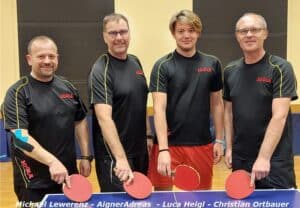 Vier Tischtennisspieler in schwarz-roten Trikots, lächelnd, zeigen Teamgeist in einer Sporthalle.
