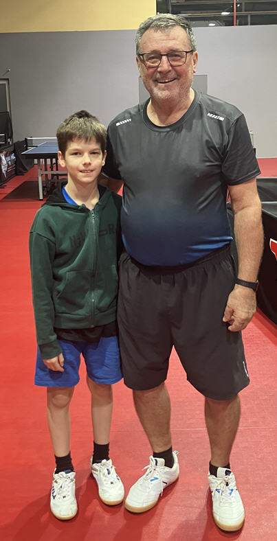 Tischtennis Leonding | Bilder „Tischtennis Leonding“ Junger Spieler und Mentor beim Tischtennis, freundlich lächelnd auf dem Sportboden.