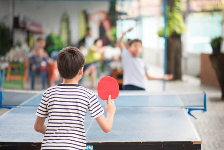 Home Kinder spielen Tischtennis im Freien mit Familie, genießen Sport und Gemeinschaft im Garten.