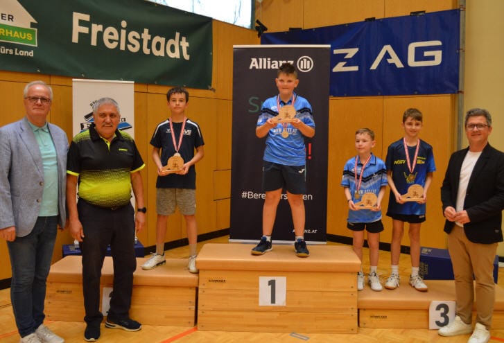 OÖTTV zeigt Stärke – Julian Luginger gewinnt U11-Titel Junge Tischtennisturnier-Gewinner auf Podium mit Medaillen und Trophäen, umgeben von stolzen Betreuern.