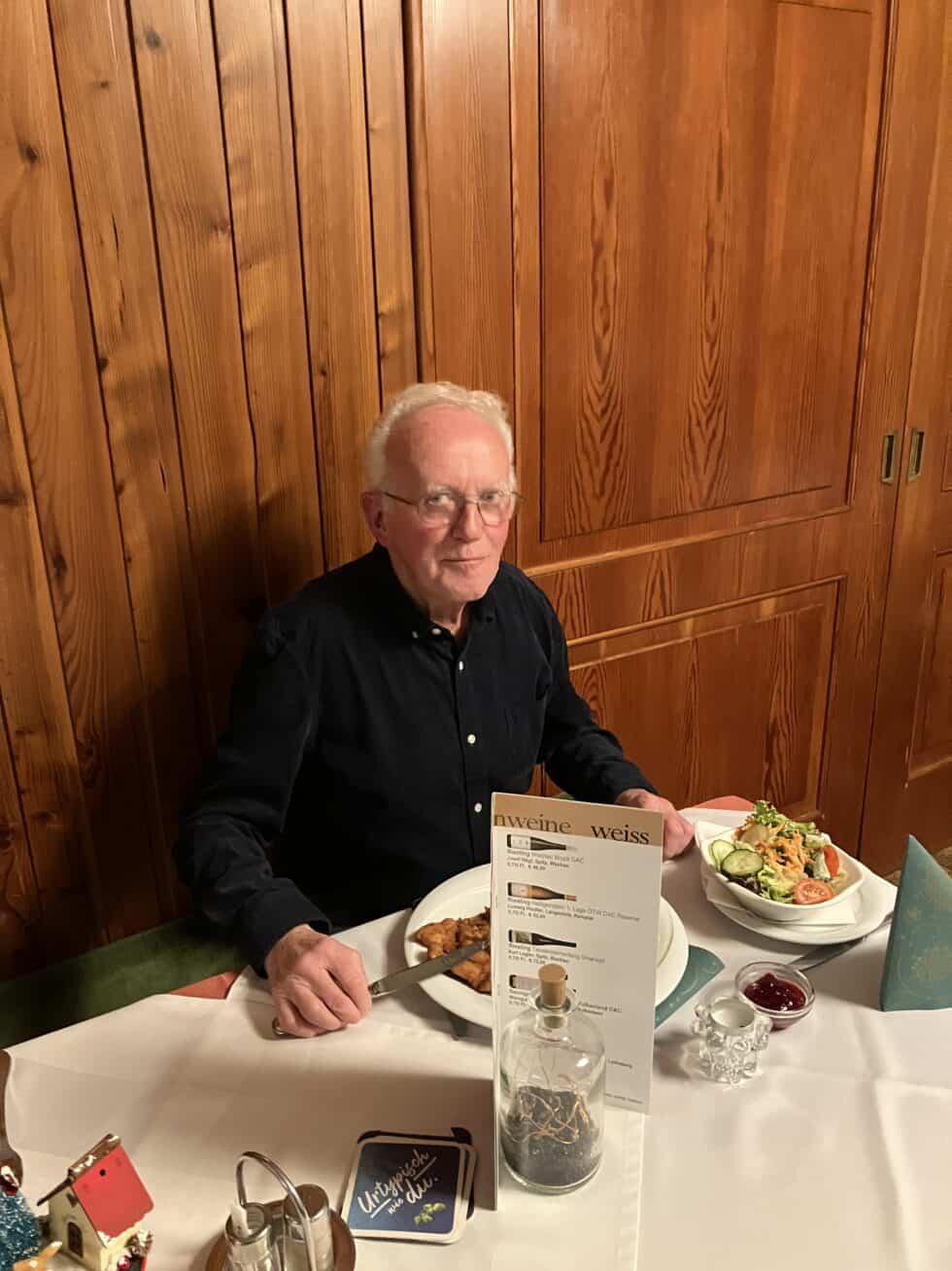 Ein älterer Mann genießt alleine ein gemütliches Abendessen in einem festlich dekorierten Restaurant.