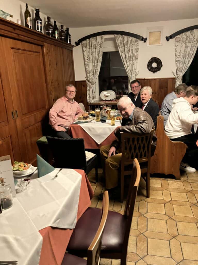 Gemütliches Gasthaus mit Holzwänden, warmem Licht und Männern beim Abendessen mit Bier und Speisen.