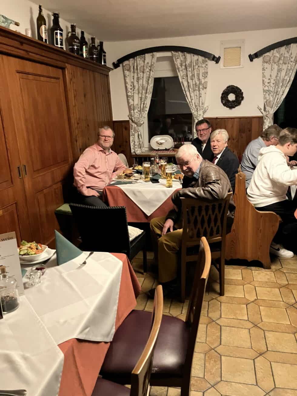 Gemütliches Gasthaus mit Holzwänden, warmem Licht und Männern beim Abendessen mit Bier und Speisen.