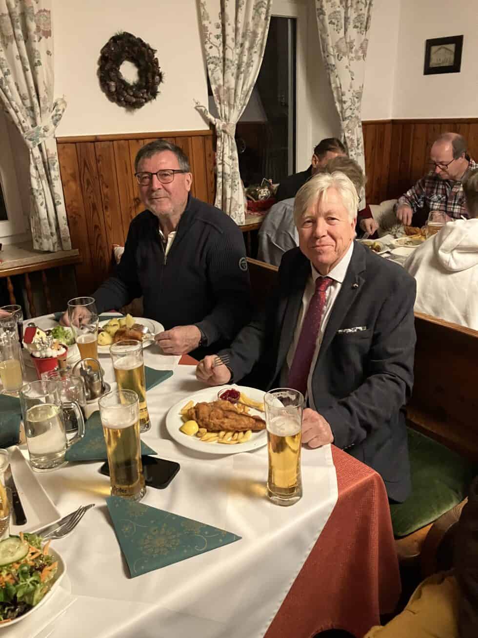 Gemütliches Abendessen: Zwei Herren genießen Schnitzel und Bier in rustikaler, festlicher Atmosphäre.