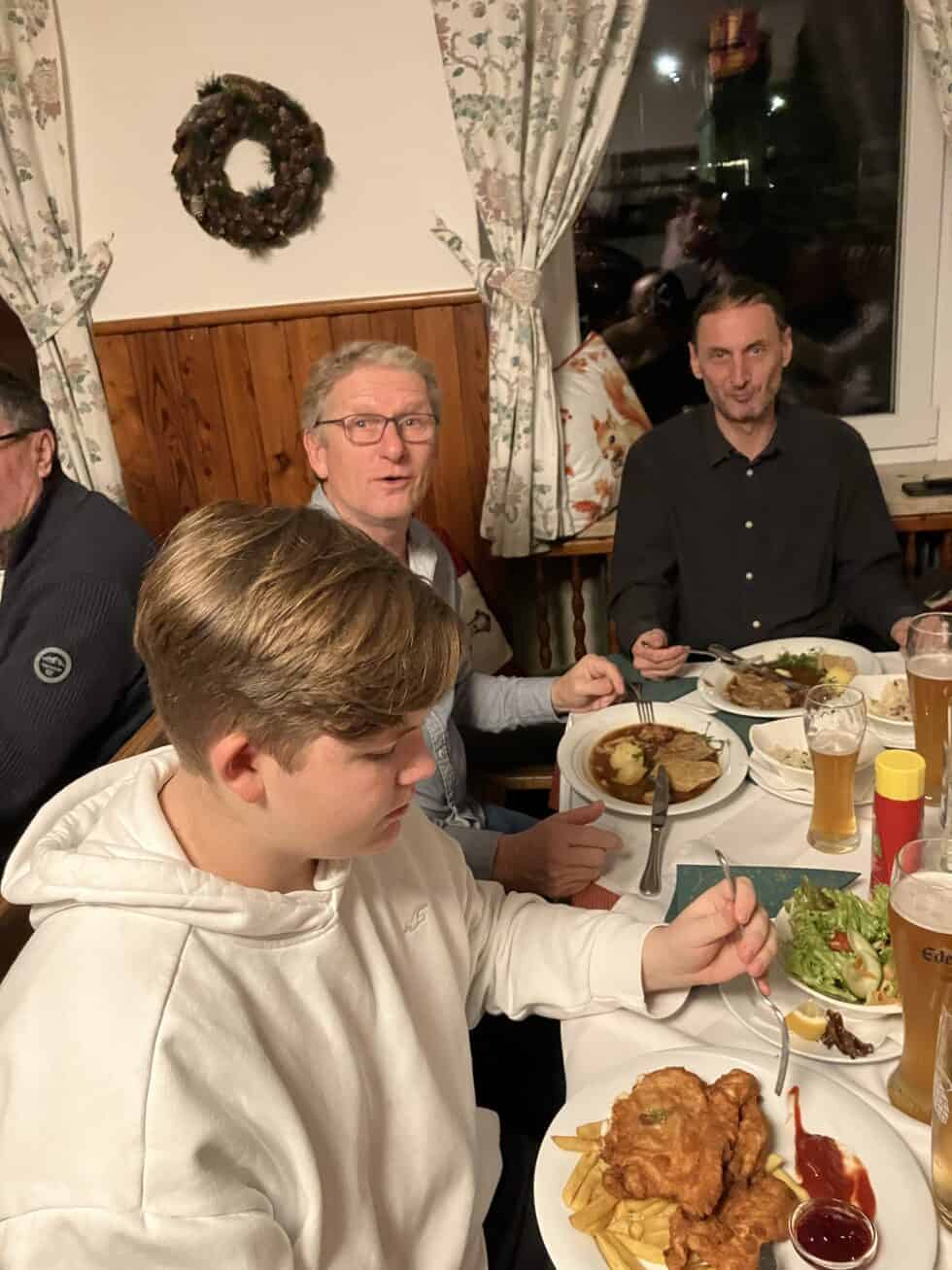 Gemütliches Abendessen mit Schnitzel, Weizenbier und Freunden in behaglicher, festlicher Atmosphäre.