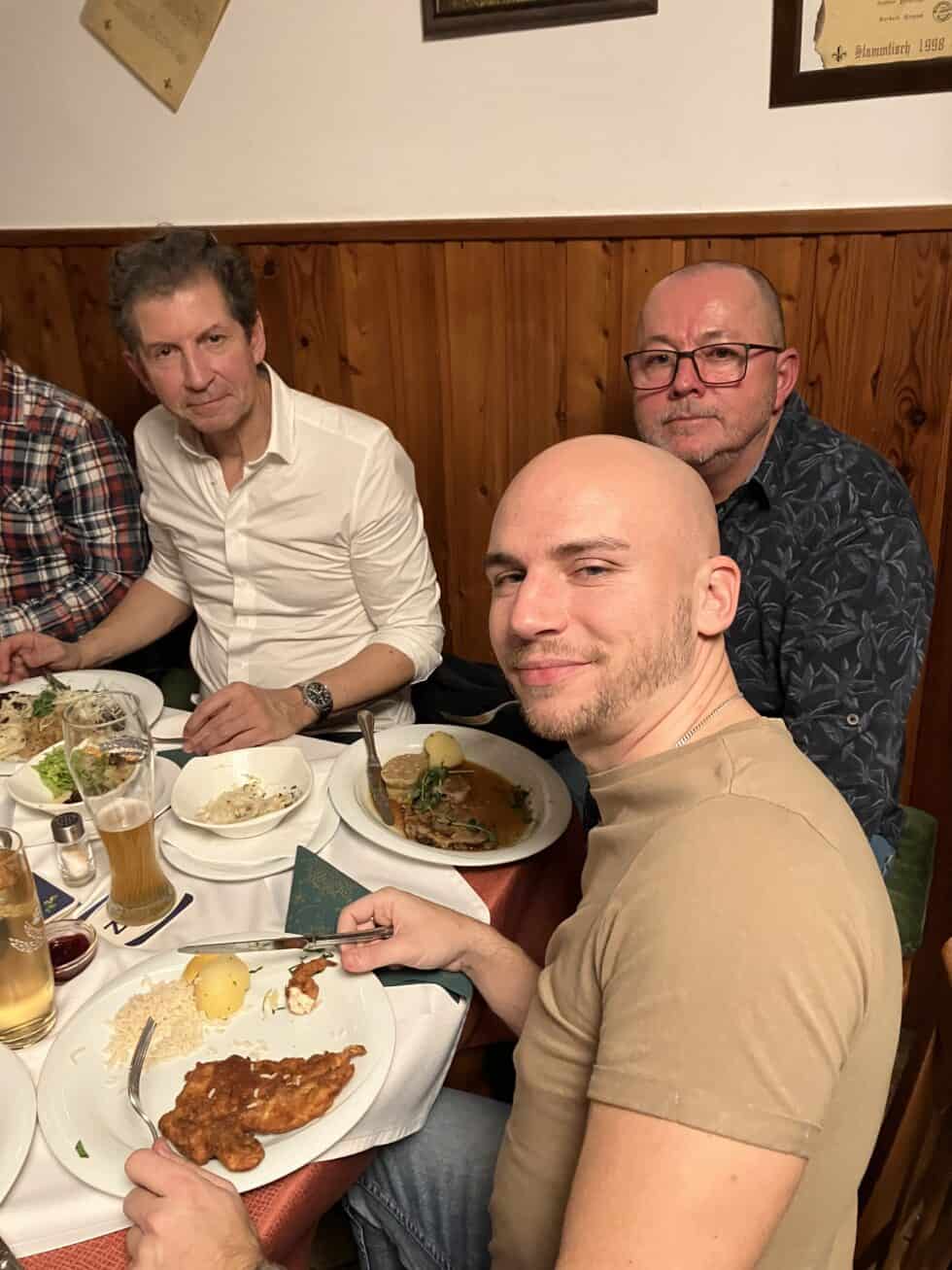 Drei Männer genießen herzhaftes Essen und Bier in einem gemütlichen, rustikalen Restaurant.