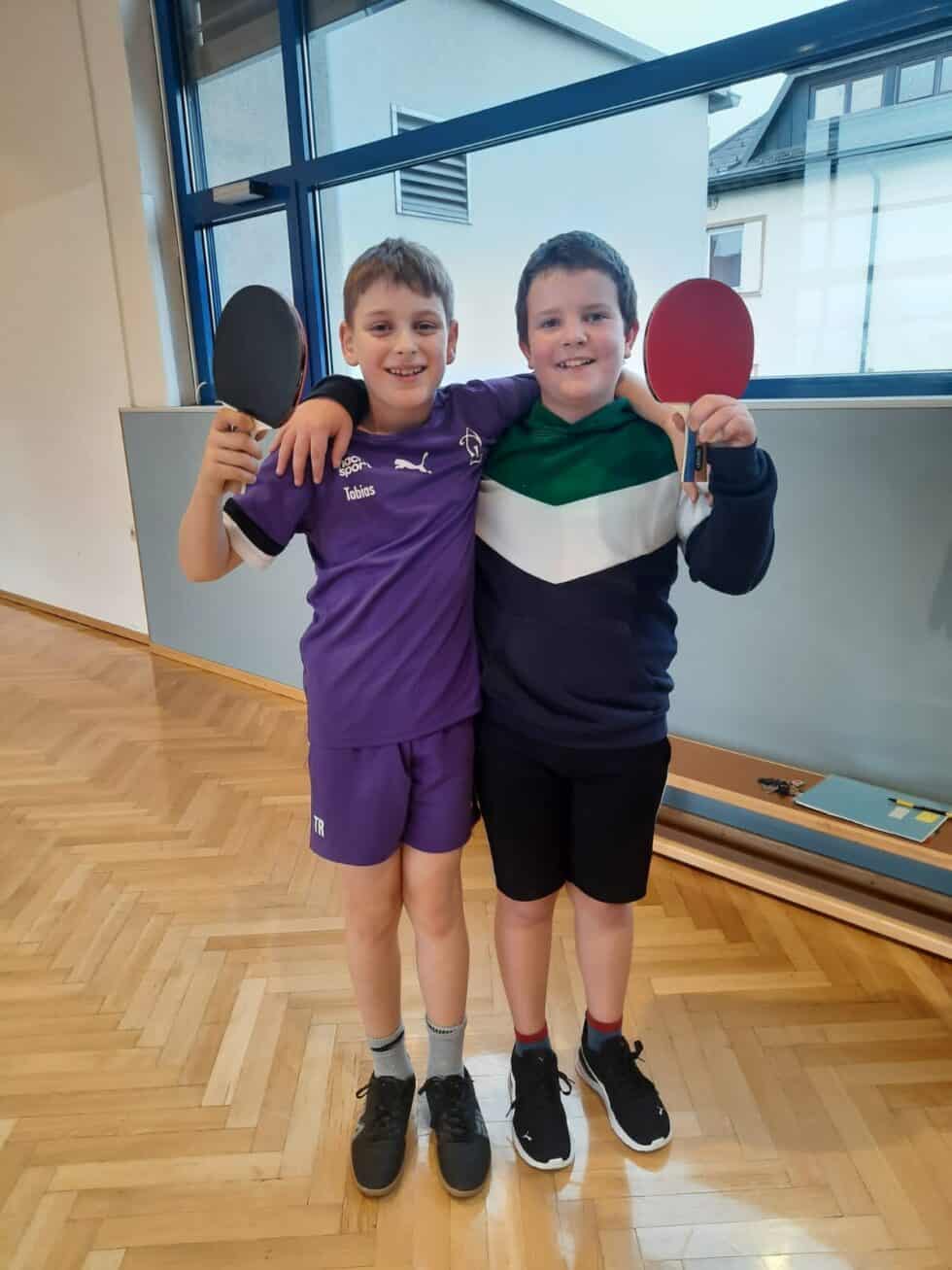 Zwei Burschen spielen Tischtennis in einer hellen Sporthalle Freundschaft und Spaß.