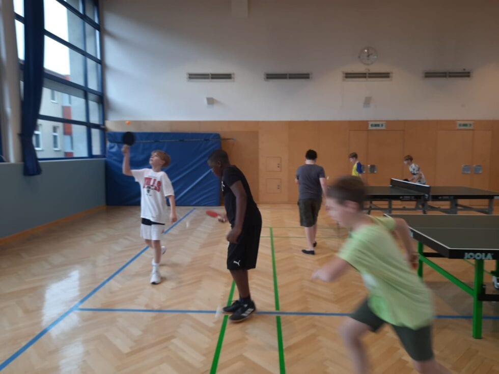 Buben spielen Tischtennis im energetischen Freizeitraum einer Schule. Freundschaftlicher Wettbewerb bei Tageslicht.