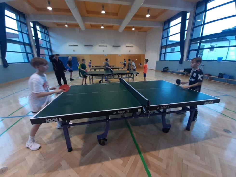 Kinder spielen Tischtennis in einem modernen Gymnasium unter Anleitung von Erwachsenen.