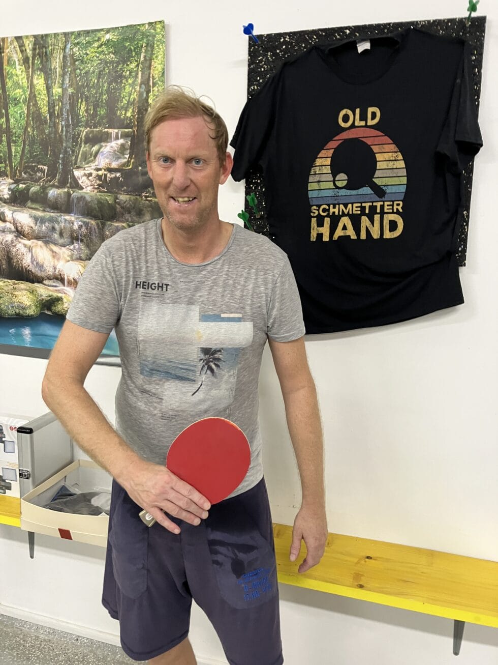 Tischtennis Leonding | Bilder „Tischtennis Leonding“ Lächelnder Mann spielt mit einem Tischtennisschläger in einem stylischen Indoor-Sportbereich.