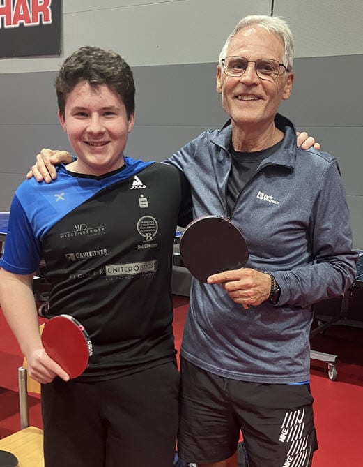 Tischtennis Leonding | Bilder „Tischtennis Leonding“ Zwei Freunde beim Tischtennis lächeln glücklich, ausdrucksvoll und sportlich gekleidet in einer Sporthalle.