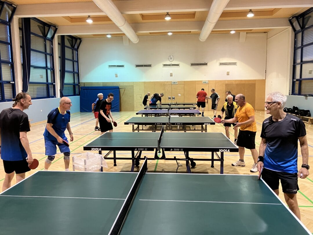 Bilder von unseren Mitgliedern Tischtennisturnier in heller Sporthalle mit zahlreichen Spielern, energetische Atmosphäre, gesellige Aktivität.