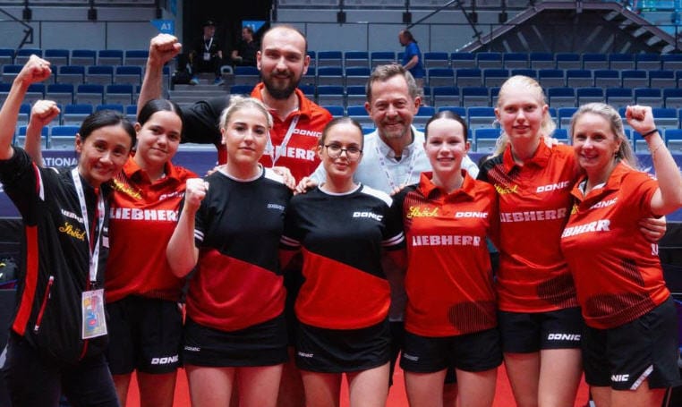 Tischtennis-Team feiert Erfolg mit Teamgeist in moderner Sportarena.