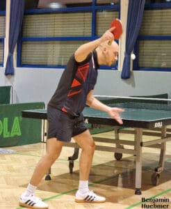 Tischtennis-Spieler konzentriert beim Aufschlag auf grünem Tisch in moderner Sporthalle.