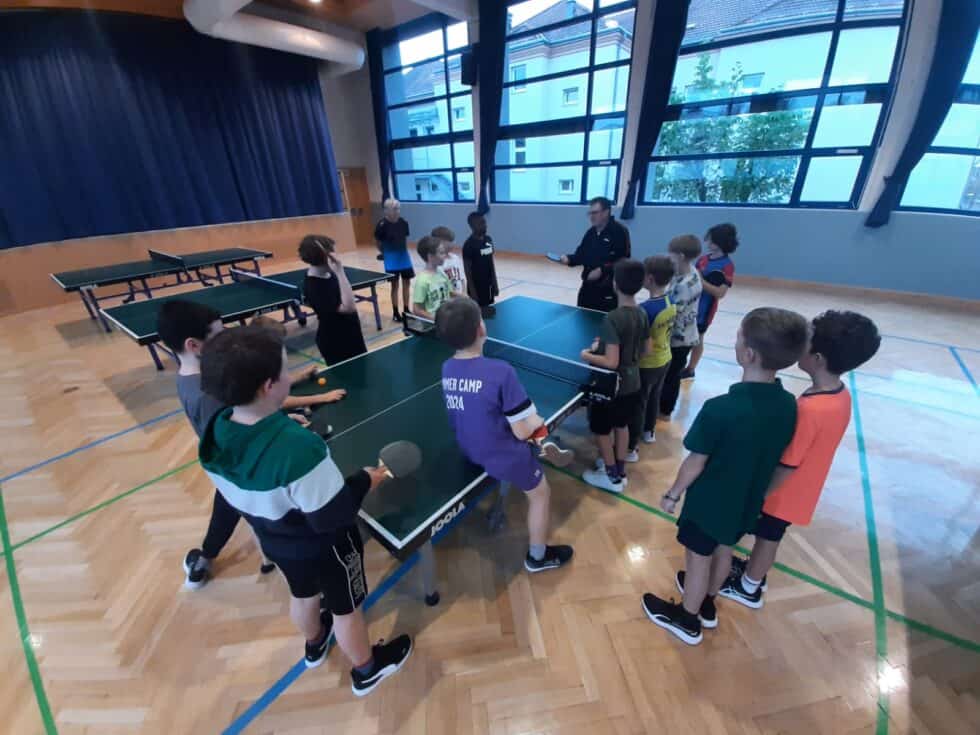 Kinder im Tischtennis Sommercamp 2024 lernen begeistert unter Anleitung eines Trainers.
