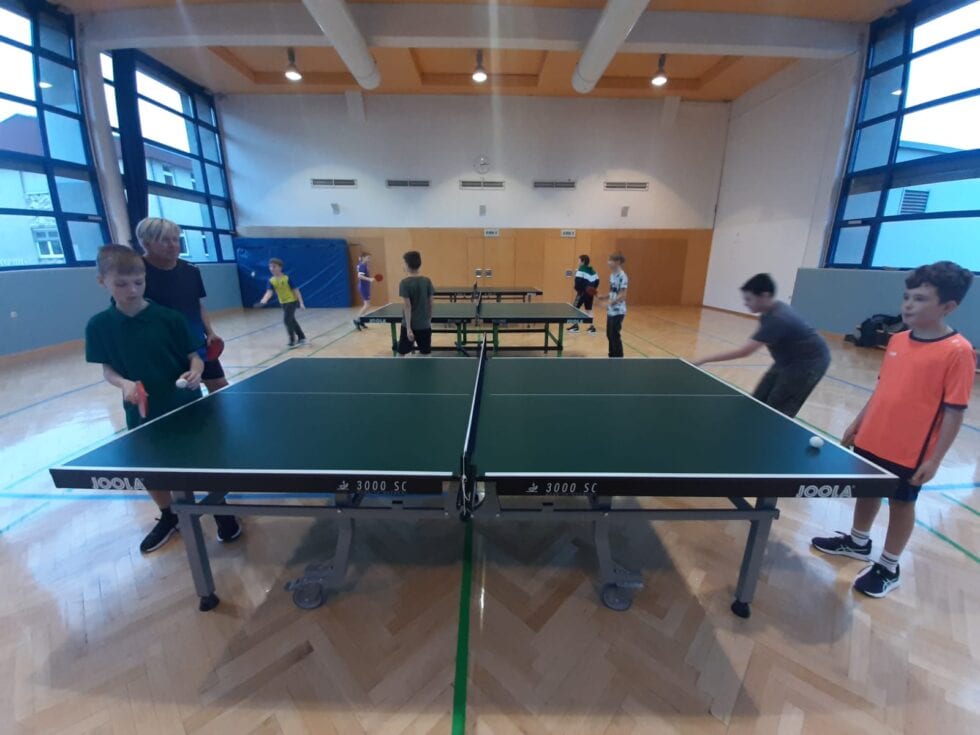 Kinder spielen konzentriert Tischtennis im hellen Turnsaal an grünen Joola 3000 SC Tischen.