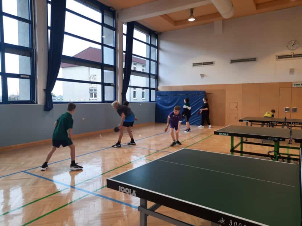 Jungen spielen Tischtennis in einer modernen, lichtdurchfluteten Sporthalle mit JOOLA-Tischen.