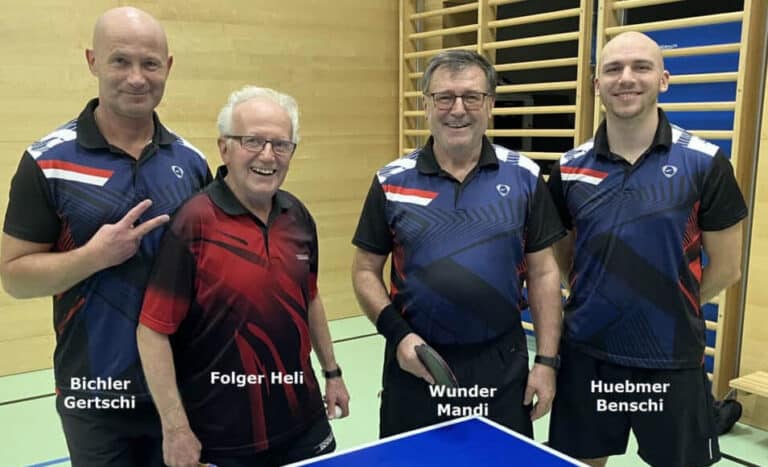 Vier Männer posieren lächelnd hinter Tischtennistisch mit Paddle, im Sportzentrum, einheitliche Trikots.