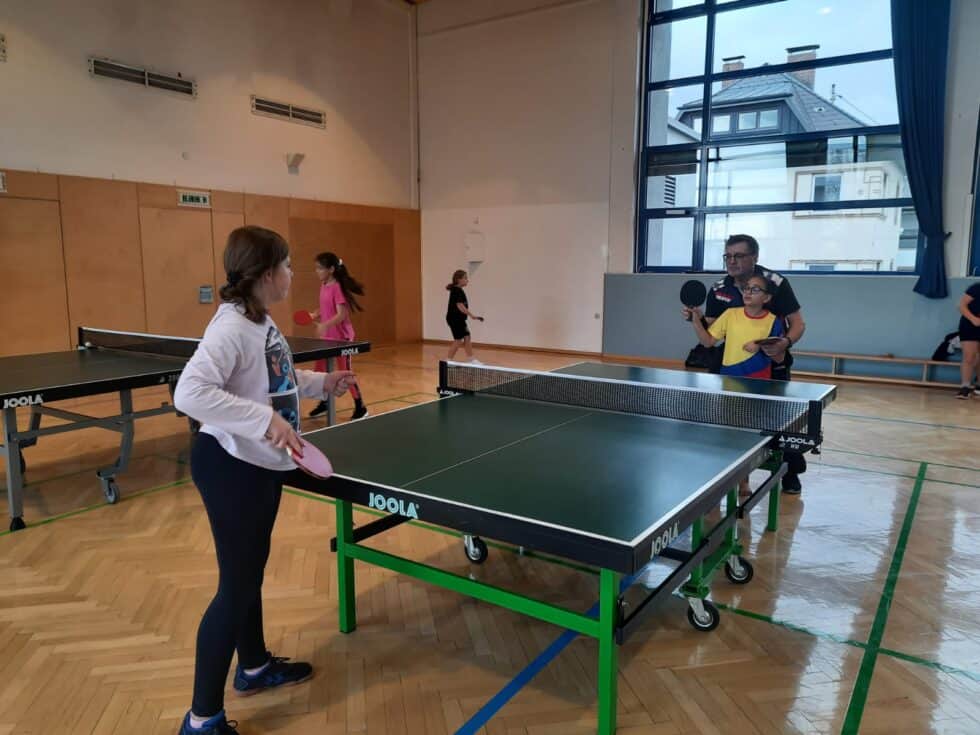 Lustiges Tischtennisspiel im Turnsaal, betreute Kinder und Erwachsene im lebendigen Gemeinschaftszentrum.