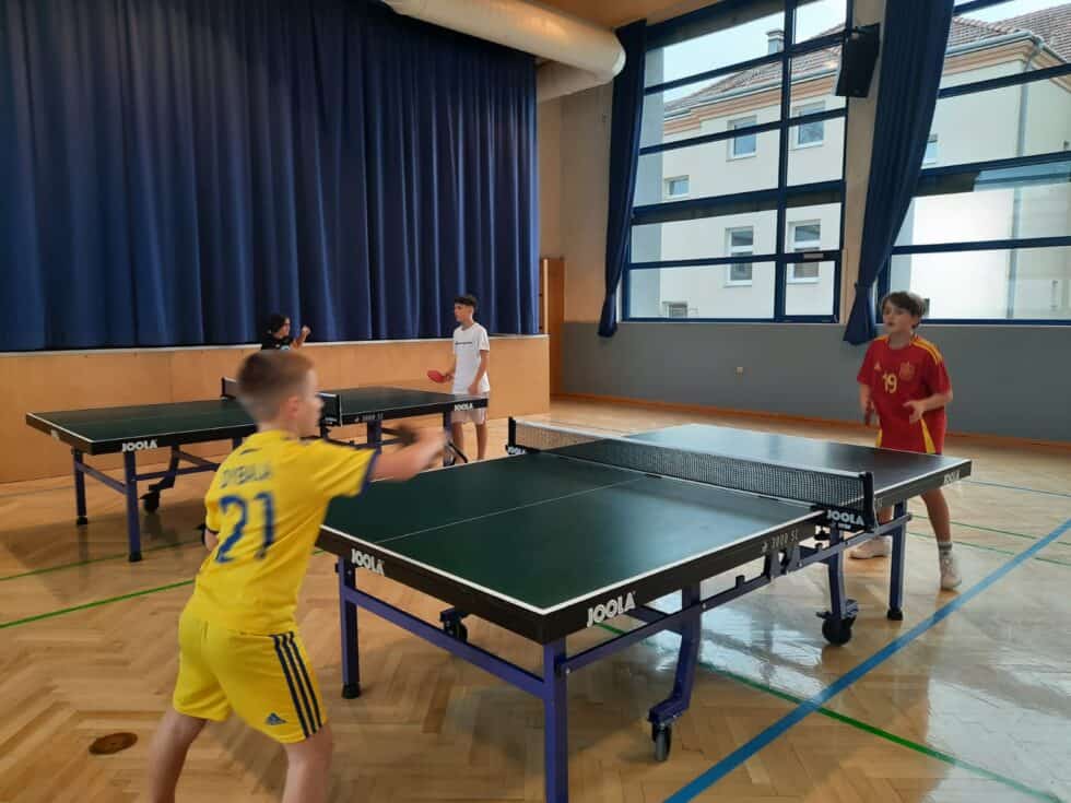 Kinder spielen Tischtennis in einer hellen Sporthalle, konzentriert und voller Begeisterung.